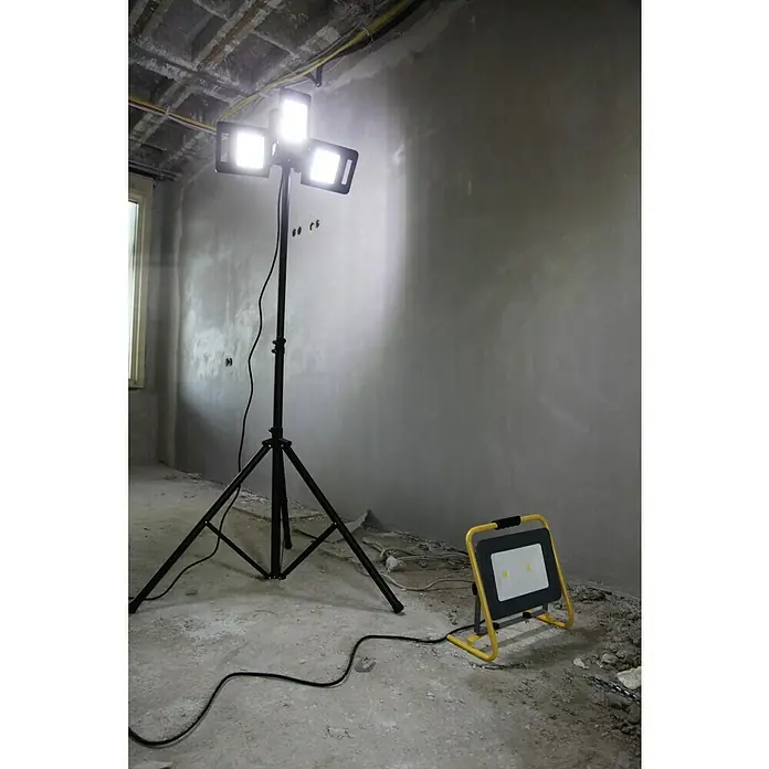 Profi Depot LED-Strahler - 8.000 lm, 6.000 K - 7.000 K, L x B x H: 1,14 x 1,32 x 2,25 m, IP54 - Das Bild zeigt eine Baustellenbeleuchtung mit einem Stativ und einer zusätzlichen Arbeitsleuchte, die einen Raum mit unverputzten Wänden ausleuchten.