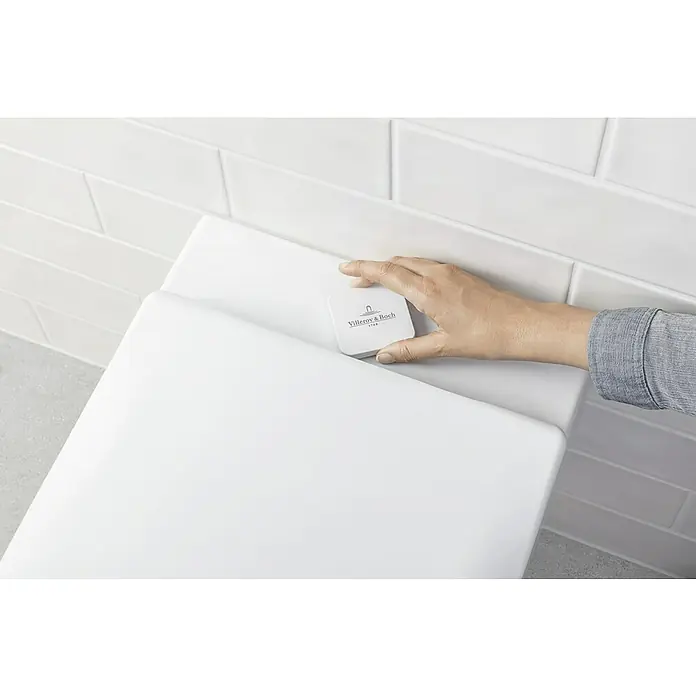 Villeroy & Boch Subway 2.0 Wand-WC ViFresh - Spülrandlos, Mit schmutzabweisender Glasur, Spülform: Tief, WC Abgang: Waagerecht, Weiß - Ein Villeroy & Boch WC-Spülknopf wird von einer Hand betätigt. Das Badezimmer verfügt über weiße Fliesen.