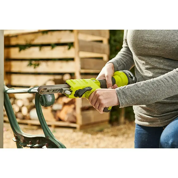 Ryobi ONE+ Akku-Bandschleifer R18PF-0 - 18 V, Ohne Akku - Eine Person verwendet einen gelben Bandschleifer, um eine grüne Parkbank im Freien zu schleifen.