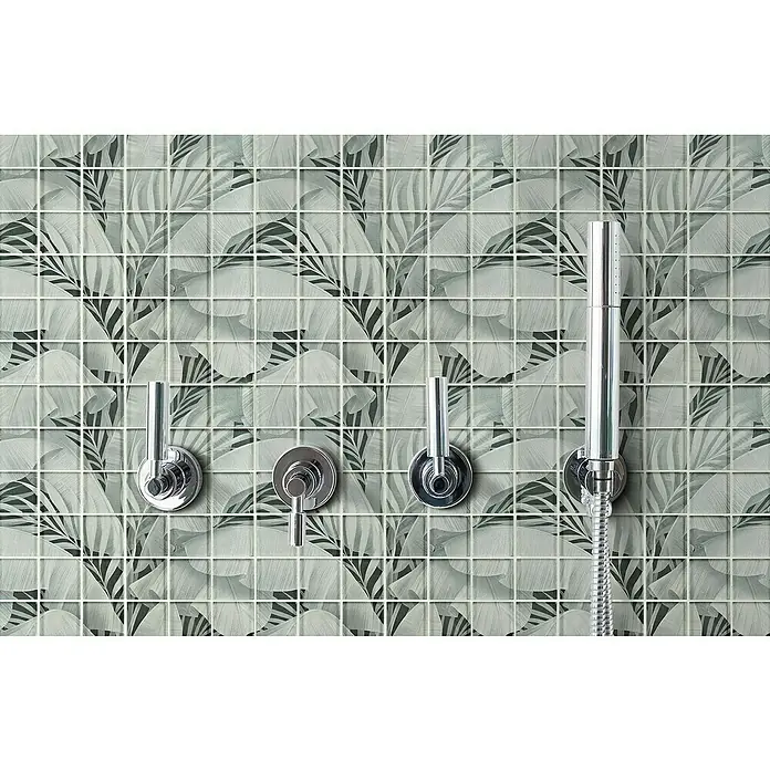 Mosaikfliese Quadrat Crystal Rainforest XCM RF03 - 29,8 x 29,8 cm, Grau, Glänzend - Detailaufnahme einer modernen Duscharmatur vor einer Wand mit floralen Mosaikfliesen. Die Armatur besticht durch ihr schlankes, chromglänzendes Design.