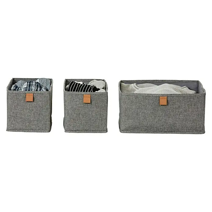 Aufbewahrungsbox-Set - 3 -tlg., Textil, Grau - Drei graue Stoffaufbewahrungskörbe in verschiedenen Größen, gefüllt mit Kleidung, mit braunen Lederetiketten.