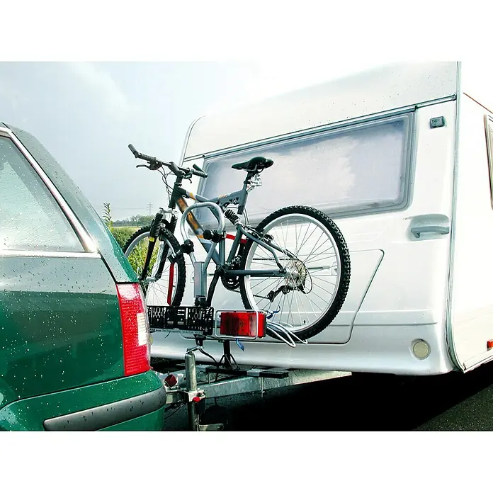 LAS Fahrrad-Aufrüst-Set - Geeignet für: Anhänger, Nutzlast: 65 kg - Ein Fahrradträger für die Anhängerkupplung mit einem montierten Fahrrad, befestigt an einem Wohnwagen und einem grünen Auto.
