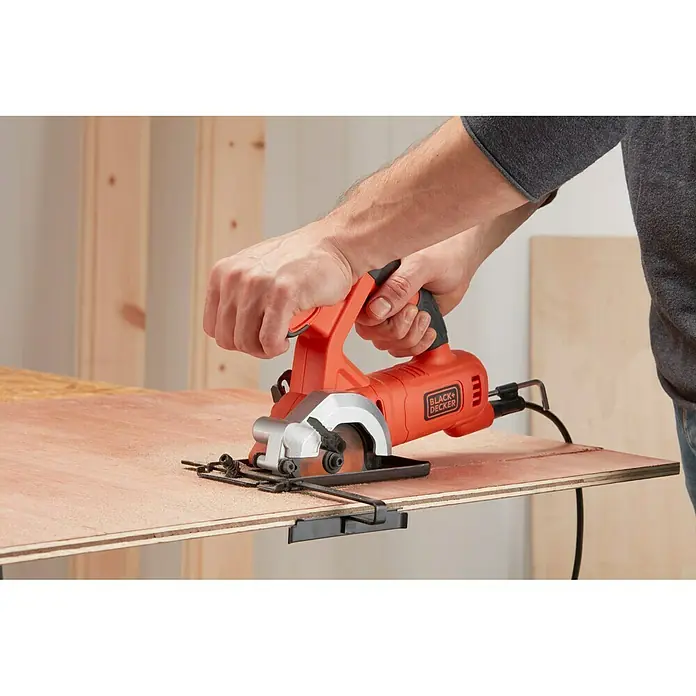 Black+Decker Minisierra circular de mano BES510-QS - 400 W, Diámetro hoja de sierra: 85 mm, Número de revoluciones de marcha en vacío: 3.600 r.p.m. - Una sierra circular Black+Decker corta una pieza de madera, con la sierra y las manos del usuario en foco.