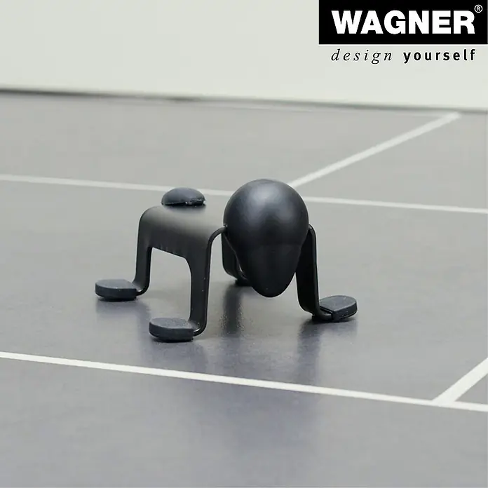Wagner System Bodentürstopper EH5208 - L x B x H: 59 x 106 x 71 mm, Stahl, Schwarz - Produktansicht eines Wagner Möbelgleiters in Form einer kleinen schwarzen Figur auf einem grauen Boden.