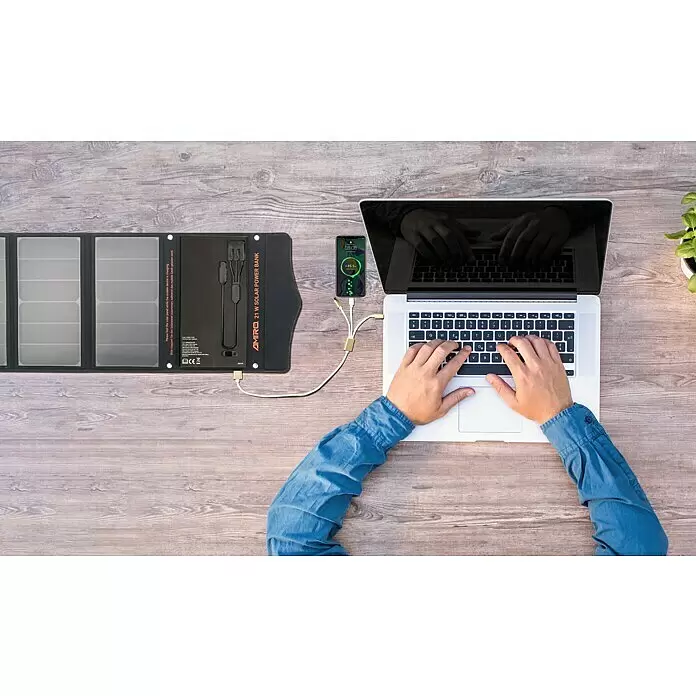 Yard Force Cargador solar LX PB21 - 48,1 Wh, 65 x 28,5 x 1,5 cm - Un power bank solar portátil negro abierto en un escritorio de madera, cargando un smartphone junto a un portátil que una persona utiliza.