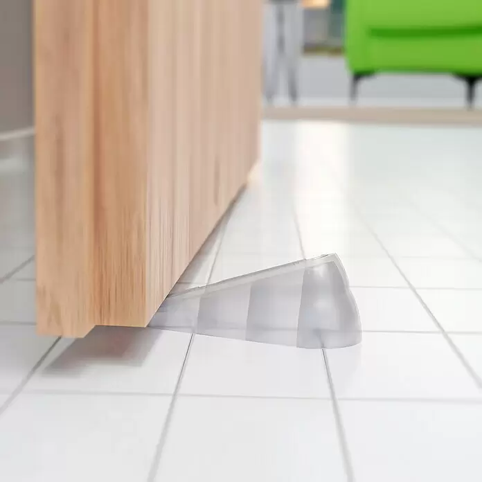 Walteco Türkeil - L x H: 100 x 36 mm, Material: Sonstiges - Transparenter Türstopper aus Kunststoff hält eine helle Holztür auf einem gefliesten Boden offen.