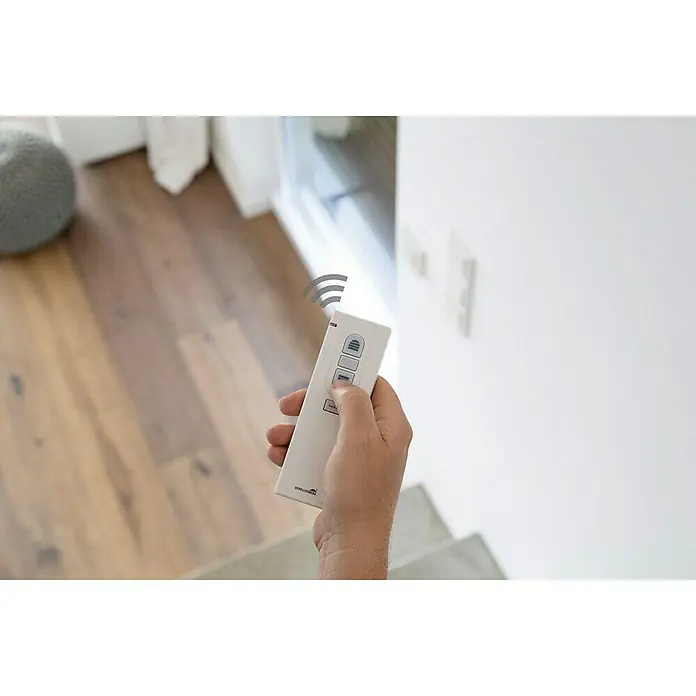 Schellenberg Smart Home Interruptor de recepción por radio - 80 x 80 x 40 mm, Blanco, Montaje enrasado - Una mano sostiene un control remoto Schellenberg blanco, que emite una señal, potencialmente para controlar dispositivos en la casa.
