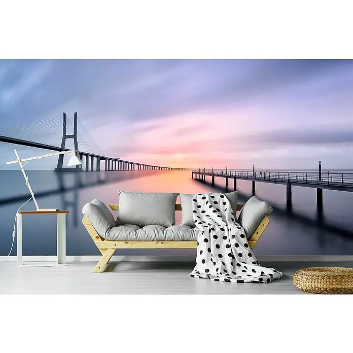 Papermoon Premium collection Fototapete Vasco De Gama - B x H: 350 x 260 cm, Vlies - Wohnzimmer mit Fototapete einer Brücke bei Sonnenuntergang, inklusive Sofa, Tischlampe und Beistelltisch.