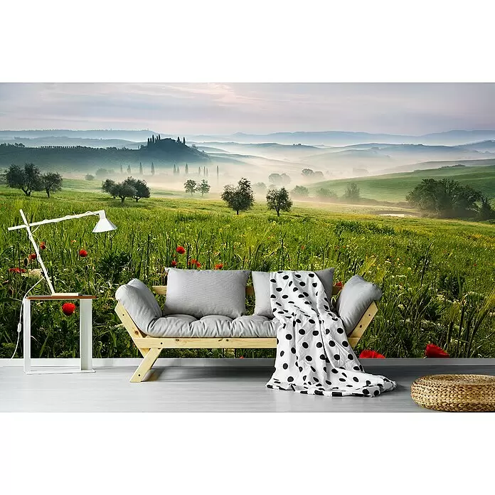 Papermoon Premium collection Fototapete Toskanischer Frühling - B x H: 500 x 280 cm, Vlies - Holzsofa mit grauen Kissen und schwarz gepunkteter Decke vor Landschaftswandbild, mit weißer Lampe und Korbschemel.