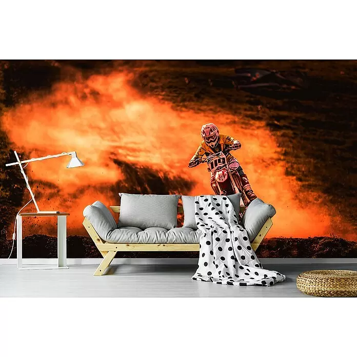 Papermoon Premium collection Fototapete Glühende Motorradstrecke - B x H: 250 x 186 cm, Vlies - Helles Holzsofa mit grauen Kissen und gepunkteter Decke, eine weiße Lampe auf einem Tisch und ein geflochtener Pouf in einem Raum mit Motocross-Wandbild.