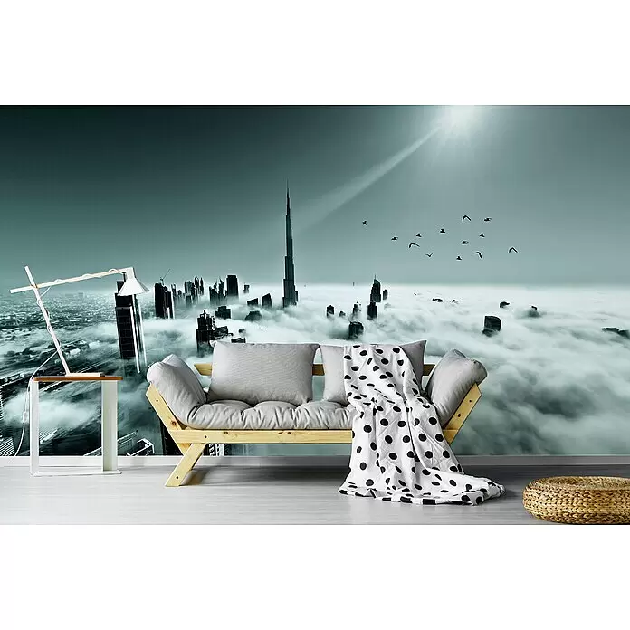 Papermoon Premium collection Fototapete Dubai - B x H: 500 x 280 cm, Vlies - Hölzernes Futon-Sofa mit hellgrauen Kissen und weißer Tupfen-Decke, in einem Raum mit dramatischer Stadt-Wandmalerei.