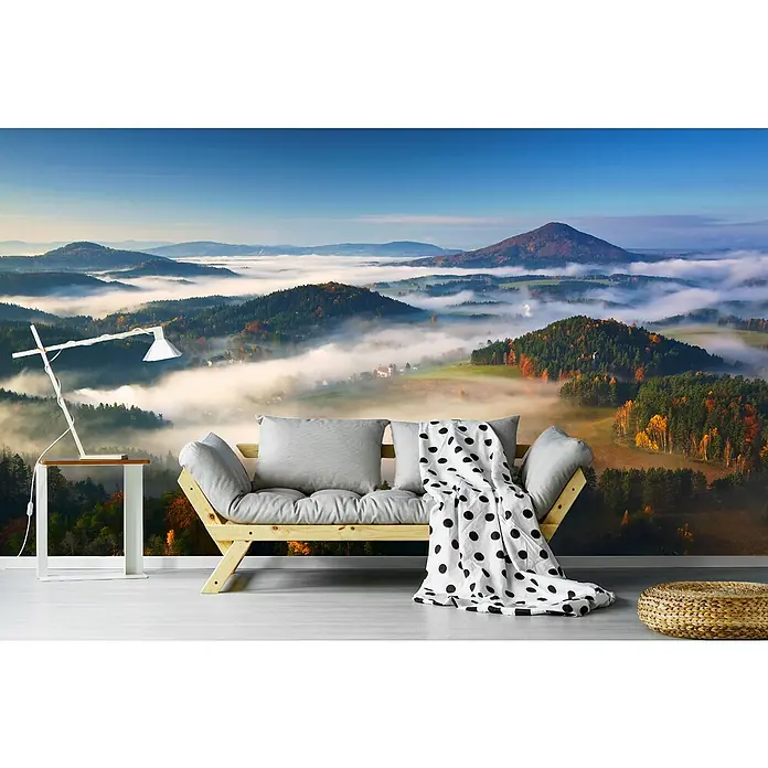 Papermoon Premium collection Fototapete Herbst Fairytale - B x H: 350 x 260 cm, Vlies - Ein gemütliches Wohnzimmer mit einem Schlafsofa, einer Lampe und einem Hocker, vor einer fotorealistischen Tapete mit Bergmotiv.