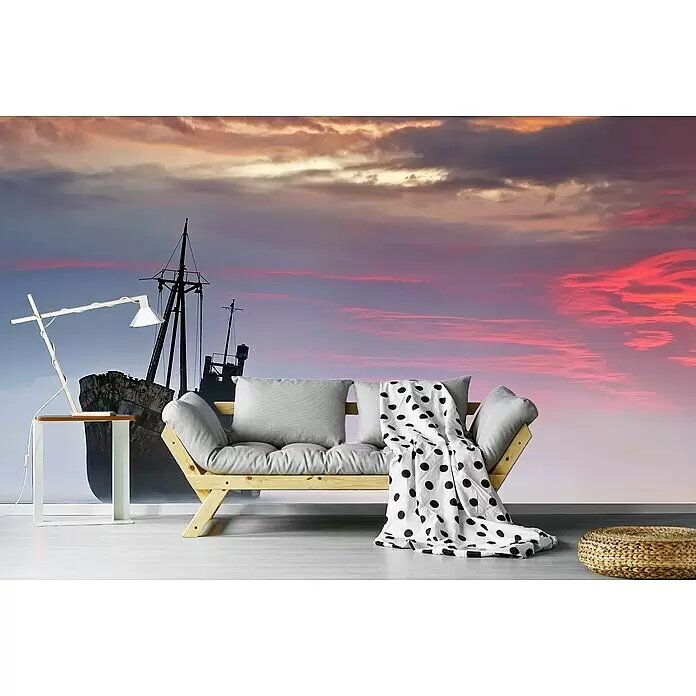 Papermoon Premium collection Fototapete Der dunkle Reisende - B x H: 400 x 260 cm, Vlies - Hölzernes Futonsofa mit hellgrauen Kissen und einer weiß gepunkteten Decke in einem Raum mit Wandbild.