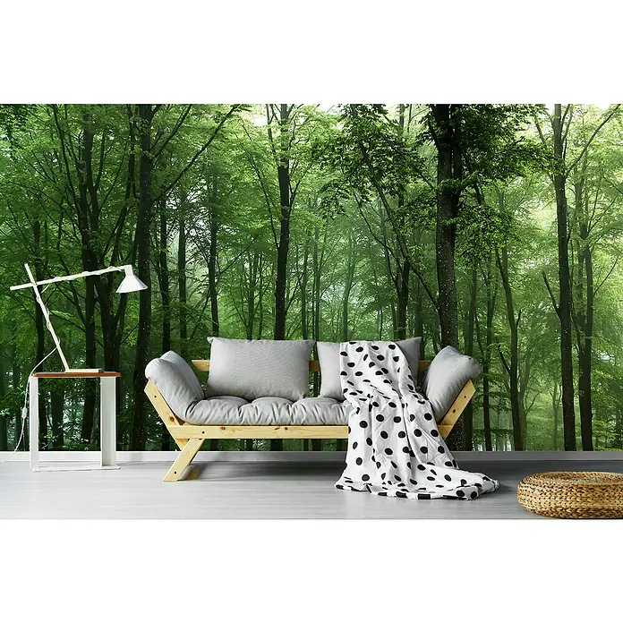 Papermoon Premium collection Fototapete Wald - B x H: 450 x 280 cm, Vlies - Ein gemütliches Sofa mit grauem Kissen und gepunkteter Decke vor einer grünen Waldtapete, ergänzt durch eine moderne Lampe und einen Hocker.