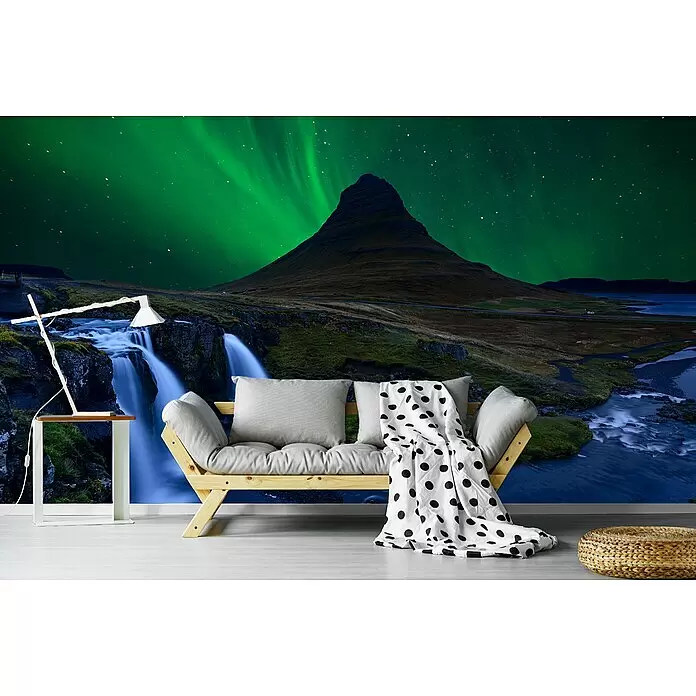 Papermoon Premium collection Fototapete Nordlichter über den Bergen, Meer und Wasserfällen - B x H: 450 x 280 cm, Vlies - Helles Holzsofa mit grauen Kissen, gepunkteter Decke, weißer Lampe, Tisch und geflochtenem Hocker in einem Raum mit Naturwandbild.