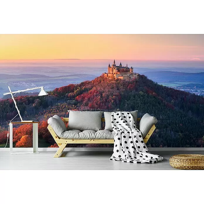 Papermoon Premium collection Fototapete Goldener Herbstabend - B x H: 500 x 280 cm, Vlies - Modernes Wohnzimmer mit grauem Futonsofa, Holzrahmen und gepunkteter Decke vor einer Burgtapete.
