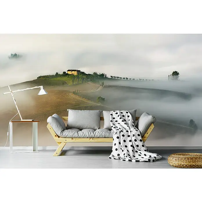 Papermoon Premium collection Fototapete Neblig abgeschottet - B x H: 450 x 280 cm, Vlies - Ein stilvolles Interieur mit einem bequemen Futon, einer eleganten Lampe und einem Hocker, vor einer malerischen Landschafts-Fototapete.