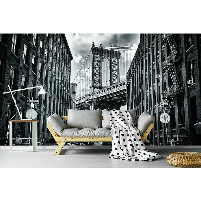 Papermoon Premium collection Fototapete In Amerika NYC - B x H: 300 x 223 cm, Vlies - Ein gemütliches Wohnzimmer mit einem stilvollen Holzbettsofa, einem Beistelltisch mit Lampe und einem dekorativen Strickhocker vor einer New Yorker Skyline Fototapete.