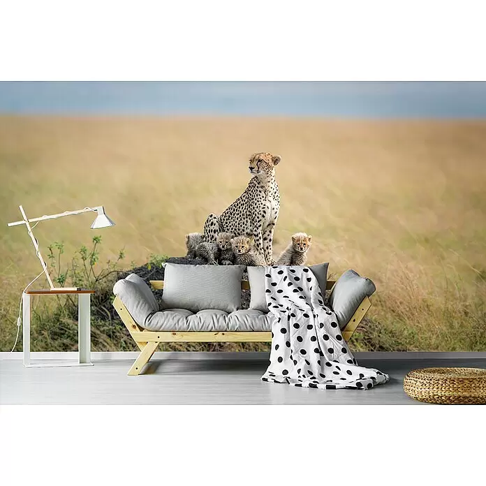 Papermoon Premium collection Fototapete Gepard Familie - B x H: 500 x 280 cm, Vlies - Holz-Futonsofa mit grauen Kissen, gepunkteter Decke, Beistelltisch mit Lampe und geflochtenem Pouf vor einem Savannen-Wandbild mit Geparden.
