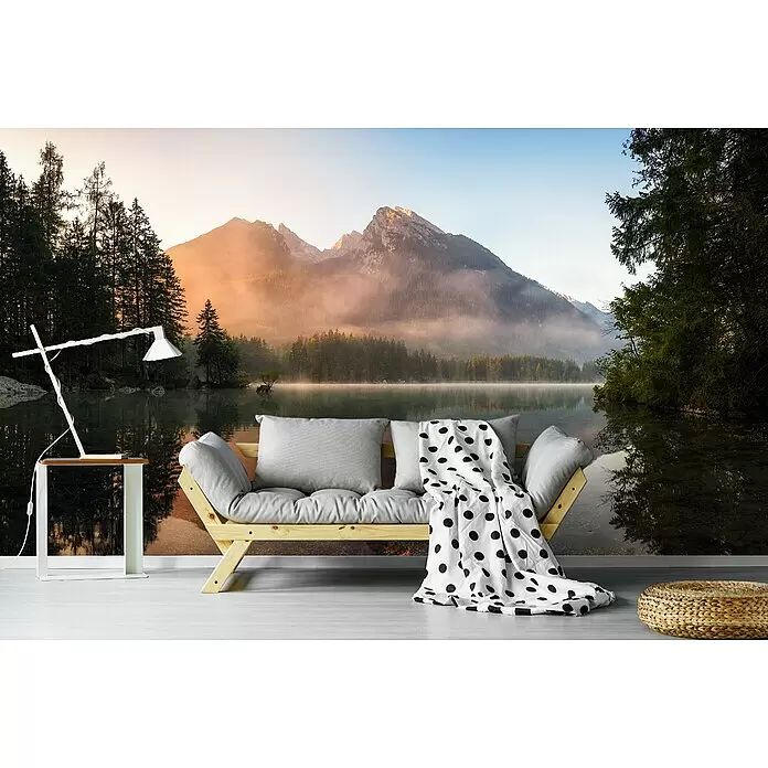 Papermoon Premium collection Fototapete Glühender Nebel - B x H: 500 x 280 cm, Vlies - Holzsofa mit grauen Kissen, gepunkteter Decke, weißem Beistelltisch mit Lampe und geflochtenem Pouf vor Naturwandbild.