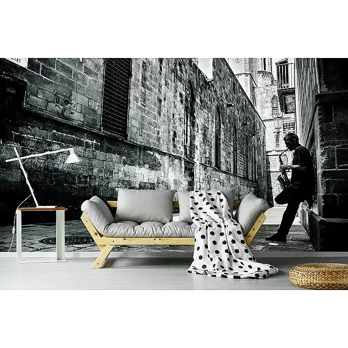 Papermoon Premium collection Fototapete Stille Straße - B x H: 450 x 280 cm, Vlies - Helles Holzsofa mit grauen Kissen und einer gepunkteten Decke, dazu ein weißer Beistelltisch und ein gewebter Pouf auf hellem Boden.