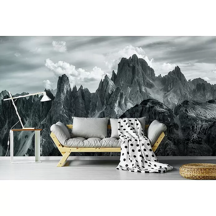 Papermoon Premium collection Fototapete Die Gipfel - B x H: 450 x 280 cm, Vlies - Schwarz-weißes Bergpanorama-Wandbild dekoriert ein Wohnzimmer hinter einem hellgrauen Sofa, Holztisch und geflochtenem Pouf.