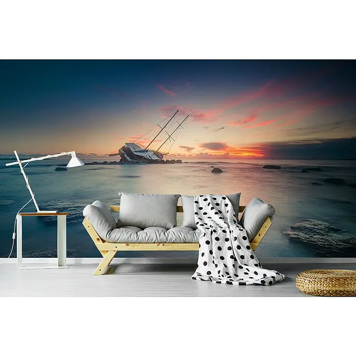 Papermoon Premium collection Fototapete Adresse - B x H: 250 x 186 cm, Vlies - Wohnzimmer mit stilvoller Dekoration. Ein Holzsofa mit Kissen und eine Lampe stehen vor einer Wandtapete mit einem gestrandeten Schiff bei Sonnenuntergang.