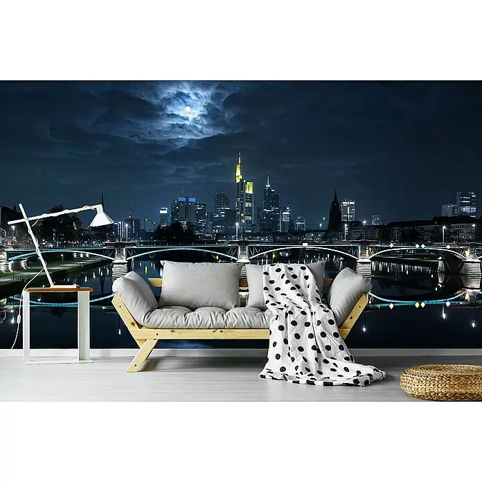 Papermoon Premium collection Fototapete Frankfurt Vollmond - B x H: 200 x 149 cm, Vlies - Helles Holzfutonsofa mit hellgrauen Kissen und einer gepunkteten Decke, in einem Raum mit nächtlicher Stadtskyline-Wandmalerei.