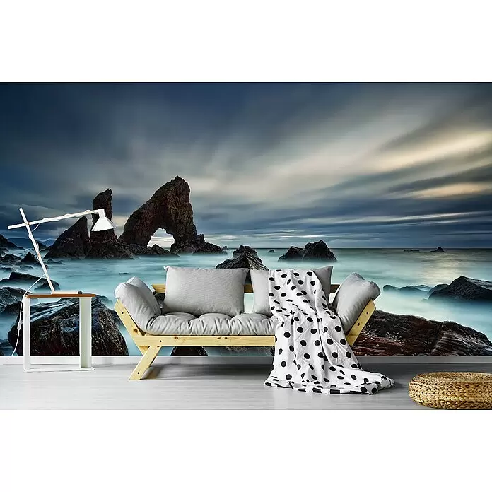Papermoon Premium collection Fototapete Seebogen Kroy-Kopf - B x H: 300 x 223 cm, Vlies - Helles Holzsofa mit grauen Kissen und gepunkteter Decke, in einem Raum mit Felsenküsten-Wandbild.