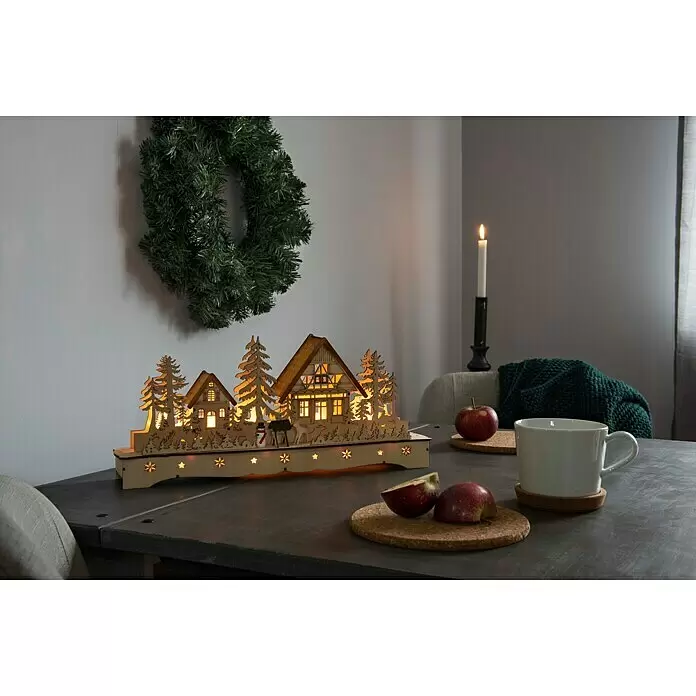 Konstsmide LED-Weihnachtsdekoleuchte Holzsilhouette Dorf mit Schneemann und Rentier - 8 x 43 x 19 cm, Braun, Batteriebetrieben, LED - Beleuchteter Holz-Lichterbogen mit Winterdorf-Szene, auf dunklem Tisch.