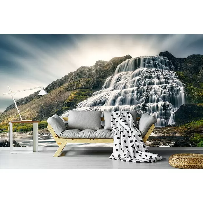 Papermoon Premium collection Fototapete Zeitlos - B x H: 500 x 280 cm, Vlies - Ein helles Holzsofa mit grauen Kissen und schwarz-weiß gepunkteter Decke, in einem Raum mit Wasserfall-Wandbild.