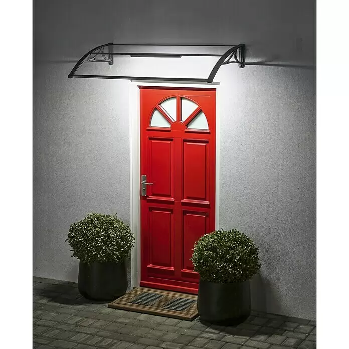 Superroof Pultvordach Formentor mit LED - 120 x 74 x 28,5 cm, Grau - Ein transparentes und schwarz gerahmtes Türvordach über einer roten Haustür, nachts beleuchtet.