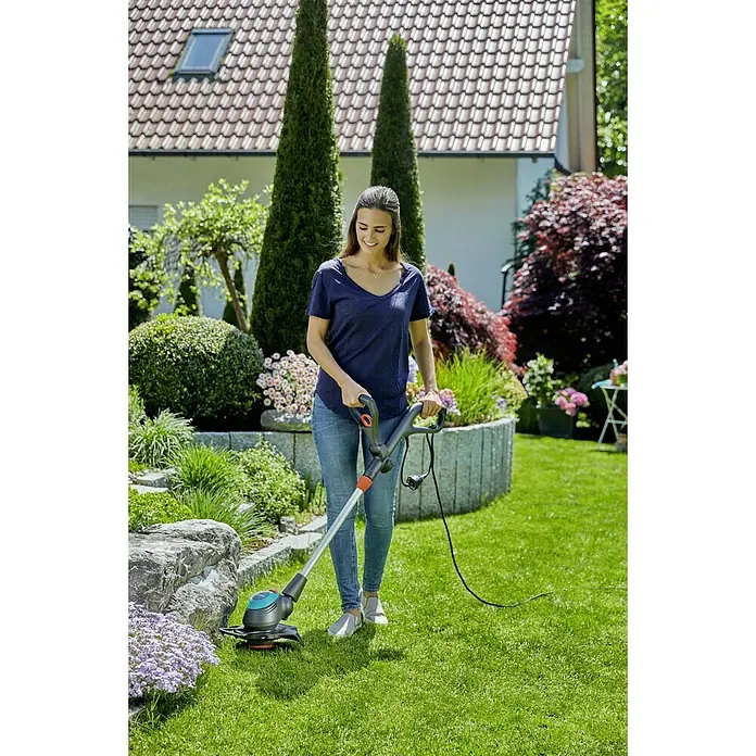Gardena Elektro-Rasentrimmer EasyCut 450/25 - 450 W, Schnittbreite Faden: 25 cm - Eine Frau arbeitet mit einem GARDENA Akku-Rasentrimmer EasyCut 23/18V P4A im Garten, um Rasen zu trimmen.
