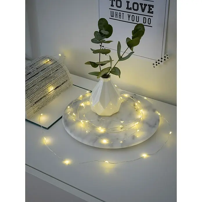 Konstsmide LED-Lichterkette - Innen, Lichtfarbe: Warmweiß, Anzahl Leuchtmittel: 40 Stk., Batteriebetrieben - Dekorative Lichterkette um eine Vase mit Eukalyptus auf einem Tisch, neben einem Buch.