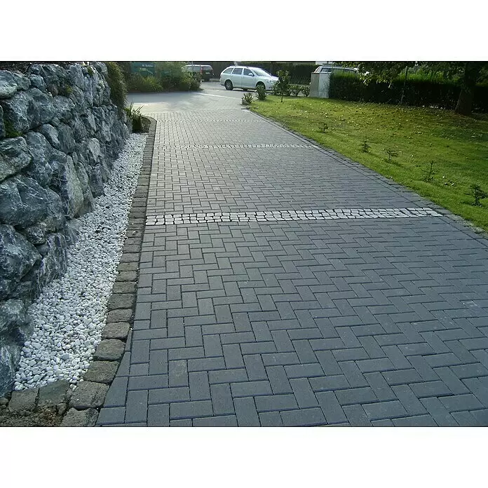 EHL Pflasterstein Rechteckpflaster mit Microfase - Anthrazit, 20 x 10 x 6 cm, Rechteckig - Grauer Rechteckpflaster-Weg mit dekorativem weißen Steinband, begrenzt von Felswand und Gras.