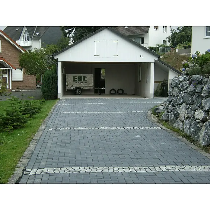 EHL Pflasterstein Rechteckpflaster mit Microfase - Anthrazit, 20 x 10 x 6 cm, Rechteckig - Eine gepflasterte Auffahrt führt zu einer Garage, in der ein Anhänger steht. Der Weg ist mit helleren Steinen akzentuiert.