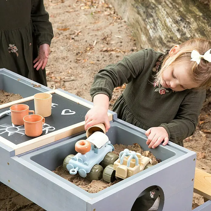 Muddy Buddy Kinder-Picknicktisch Creator - L x B x H: 100 x 90 x 50 cm, Holz, Natur/Wolkengrau - Mädchen spielt mit Sandkastenspielzeug in einer grauen Outdoor-Spielküche mit Tafel.