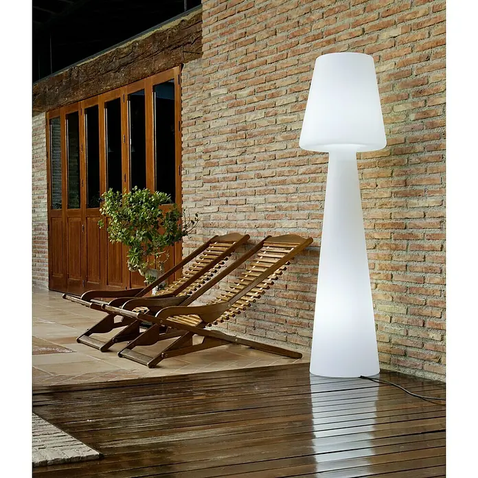 New Garden Lámpara de diseño para exterior LED Lola - 8 W, Blanco frío, Altura: 165 cm - Lámpara de pie blanca en el exterior junto a dos tumbonas de madera y una pared de ladrillo. La lámpara brilla intensamente, emitiendo una luz suave.