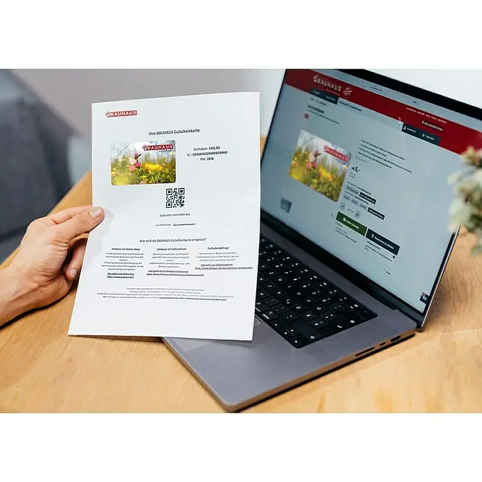 Gutscheinkarte - Zum Selbstausdruck, Gutscheinwert: Individueller Betrag, Frühlingswiese - Einlösbarer Bauhaus-Gutschein im Wert von 60,00 € neben einem Laptop, der die Bauhaus-Website mit Geschenkkarten zeigt, ideal als Geschenk.