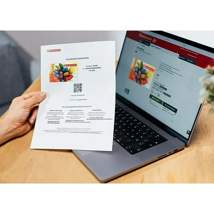 Gutscheinkarte - Zum Selbstausdruck, 20 Euro, Bunte Pinsel - Bauhaus Gutscheinkarte mit einem Wert von 60 Euro wird vor einem Laptop gehalten, der die Bauhaus Webseite anzeigt, ideal für Heimwerker.