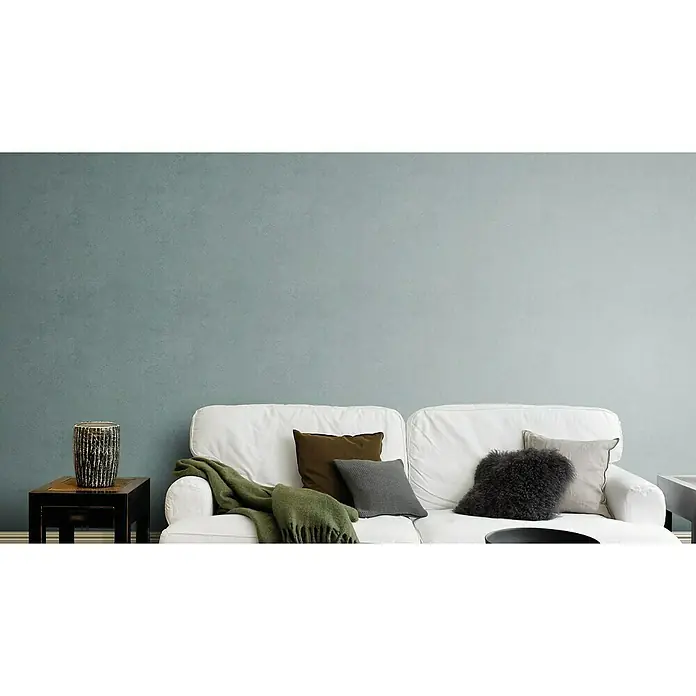 Rasch Factory V Vliestapete - Grün, Uni, 10,1 x 0,53 m - Wohnzimmergestaltung mit einem weißen Sofa, Kissen und einer grünen Decke vor einer strukturierten Wand.