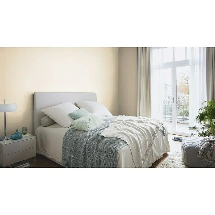 Rasch Indian Style Vliestapete - Beige, Uni, 10,1 x 0,53 m - Einladendes Schlafzimmer mit einem komfortablen Bett, das mit weichen Kissen und einer stilvollen Tagesdecke ausgestattet ist, ideal für erholsame Nächte.