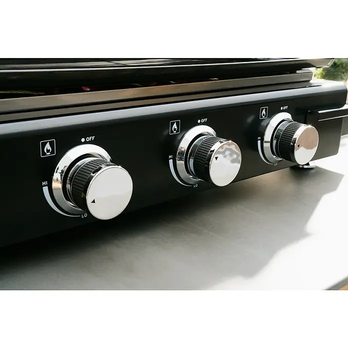 Kingstone Barbacoa de gas Nebraska - Superficie de la parrilla (An x Pr): 63,5 x 31 cm, Número de quemadores: 3 - Primer plano de una parrilla negra con tres botones de control para los niveles de calor, de "LO" a "HI", y "OFF" para regular la potencia.