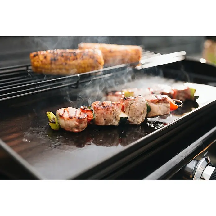 Kingstone Barbacoa de gas Nebraska - Superficie de la parrilla (An x Pr): 63,5 x 31 cm, Número de quemadores: 3 - Brochetas de carne a la parrilla y mazorcas de maíz chisporrotean en una parrilla negra, con humo.