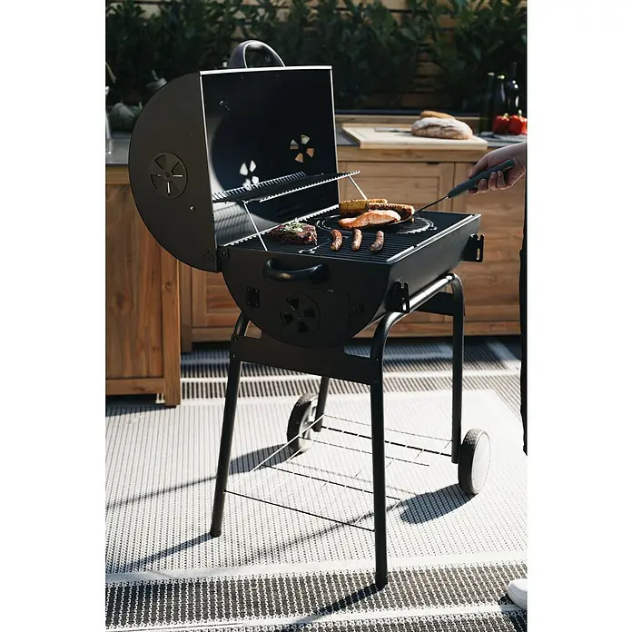 Kingstone Grillbesteck Set - 2 -tlg. - Ein Holzkohlegrill mit geöffnetem Deckel, auf dem sich Grillgut befindet, steht auf einer Terrasse bereit für das Barbecue.