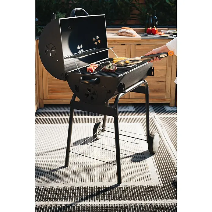 Kingstone Grillzange - Länge: 46 cm - Ein Holzkohlegrill mit aufgeklapptem Deckel, auf dem Würstchen, Steak und Maiskolben brutzeln, während eine Person mit einer Zange hantiert.