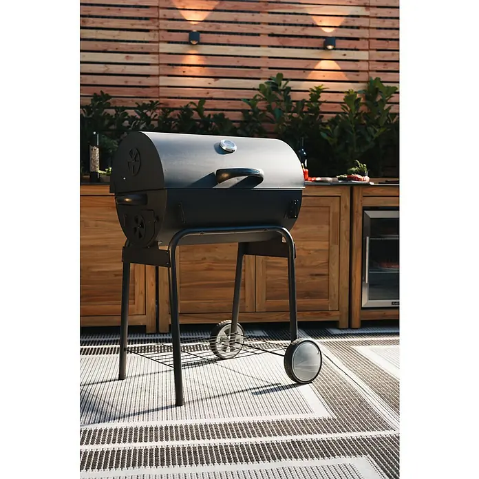 Grillstar Holzkohlegrill GrilltonneB x T x H: 109 x 71 x 87 cm, Grillfläche (B x T): 64 x 43 cm, Schwarz - Nahaufnahme eines Holzkohlegrills mit Deckel auf einem gestreiften Teppich im Freien, ideal für sommerliche Grillabende.