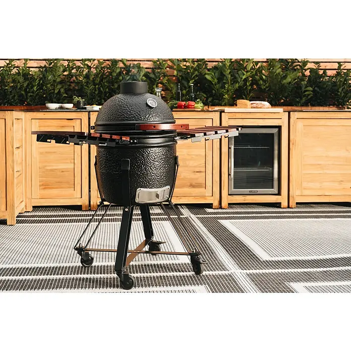 Kingstone Holzkohlegrill Kamado 38 - Durchmesser Grillfläche: 38,3 cm, Schwarz - Ein schwarzer Kamado-Grill mit Holzakzenten steht auf einer Terrasse neben einer Außenküchenzeile mit Holztüren und einem Kühlschrank.