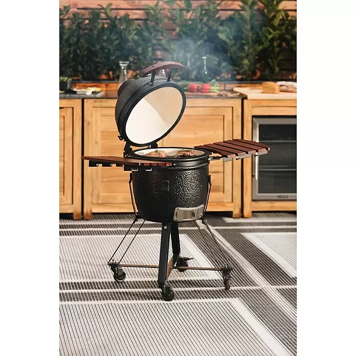 Kingstone Holzkohlegrill Kamado 38 - Durchmesser Grillfläche: 38,3 cm, Schwarz - Schwarzer Kamado-Grill mit geöffnetem Deckel, der Fleisch auf dem Rost zeigt, umgeben von Holzküchenschränken im Freien.
