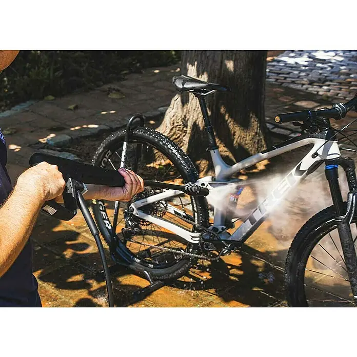 Koma Tools PRO Series Hidrolimpiadora de alta presión - 120 bar, 1.400 W, Capacidad de bombeo: 432 l/h - Lavadora a presión en uso para limpiar una bicicleta de montaña Trek de suciedad. La bicicleta se está limpiando frente a un árbol.
